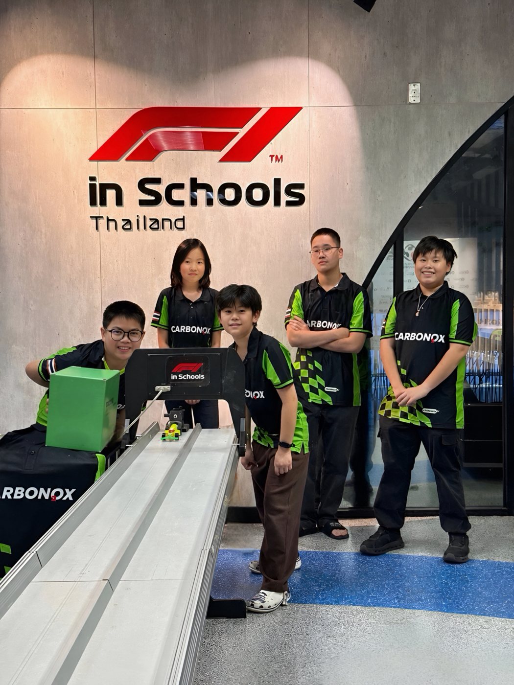 The five CARBONOX team members in team shirts beside the F1 in Schools Thailand start gate and track